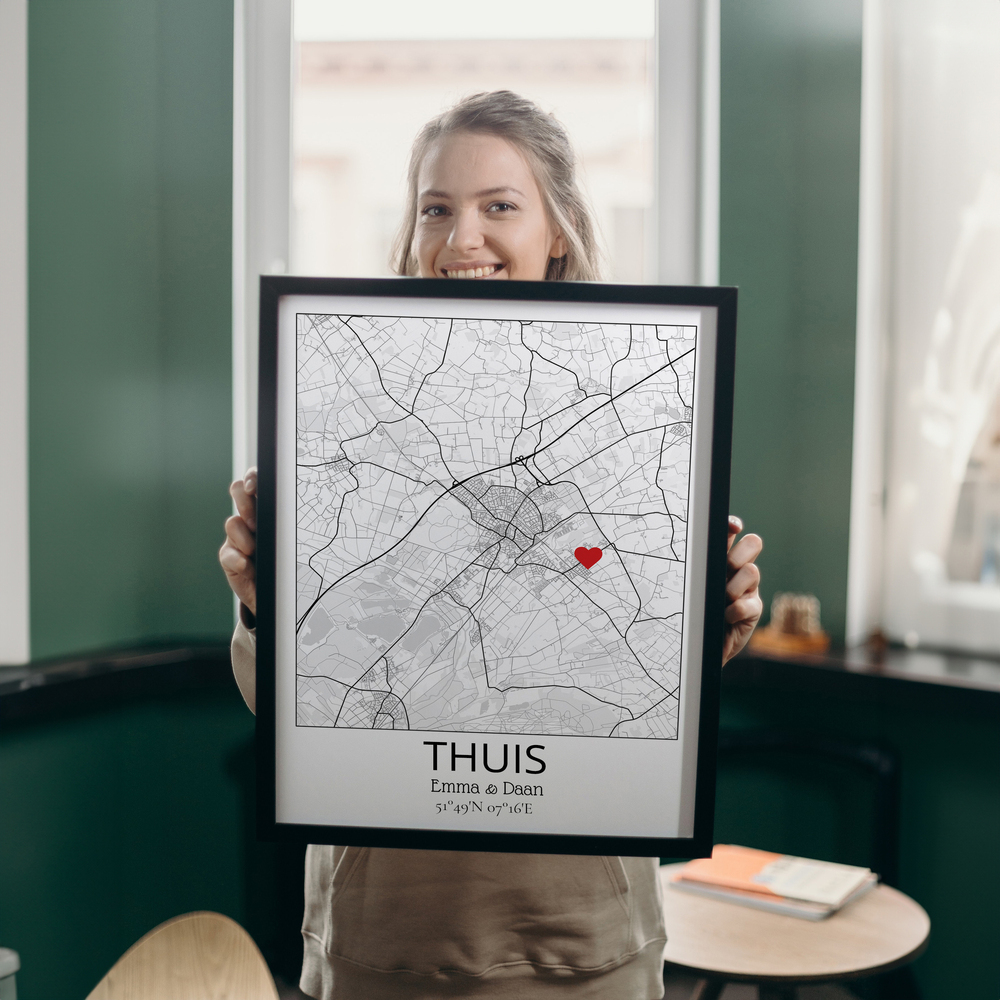 Zwart-witte stadskaart in zwarte lijst met rood hartje bij het woonadres, gepresenteerd in een ruimte met groene muren